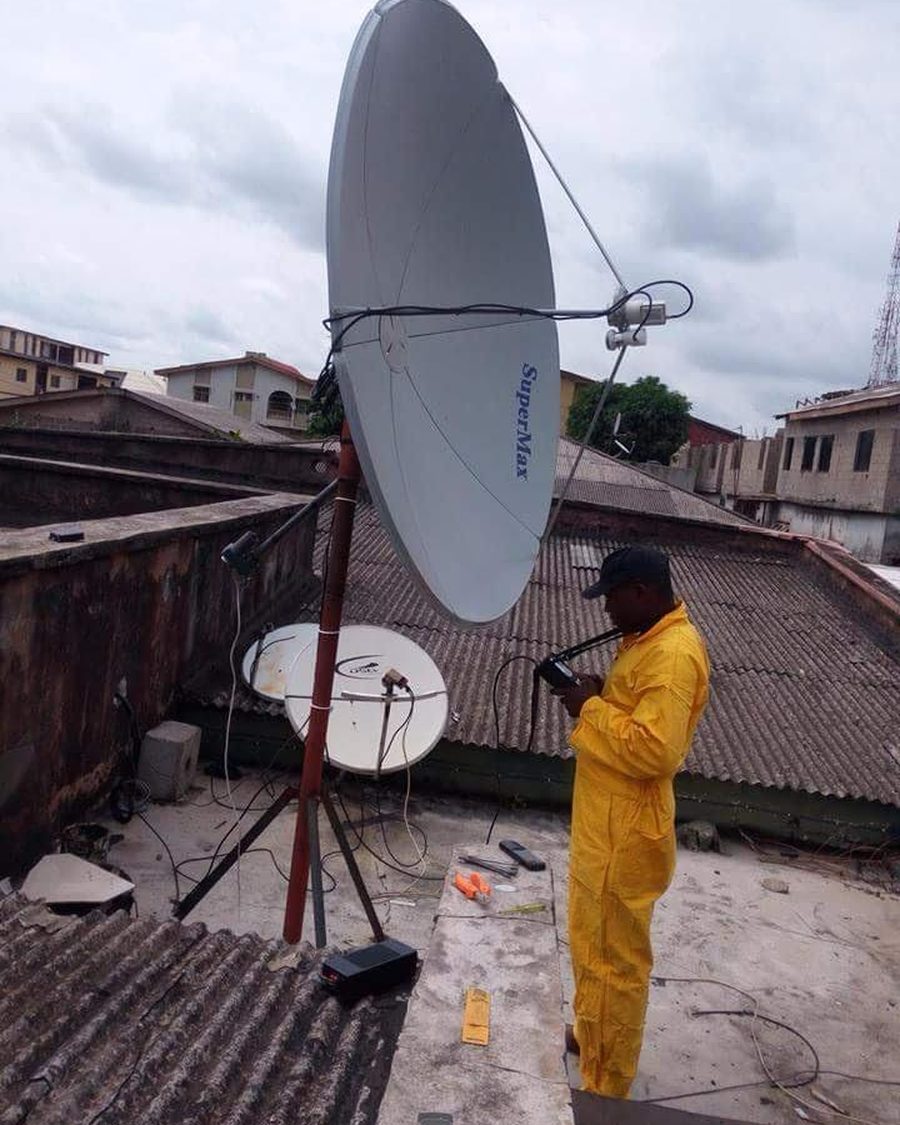 A technician in yellow overalls aligning a SuperMax satellite dish on a rooftop.
